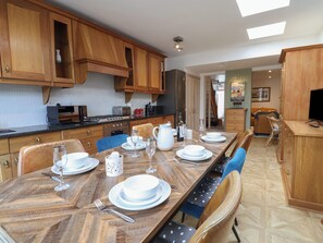 A dining area with a long wooden table set for four, surrounded by wooden cabinets and a kitchen in the background. - Old Harbour Townhouse (Weymouth)