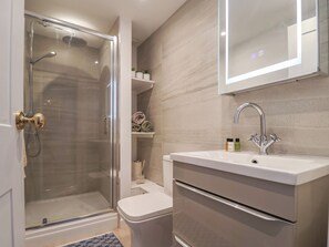 A modern bathroom with a glass-enclosed shower, a white sink with a mirror above it, and a small shelf with toiletries. - Old Harbour Townhouse (Weymouth)