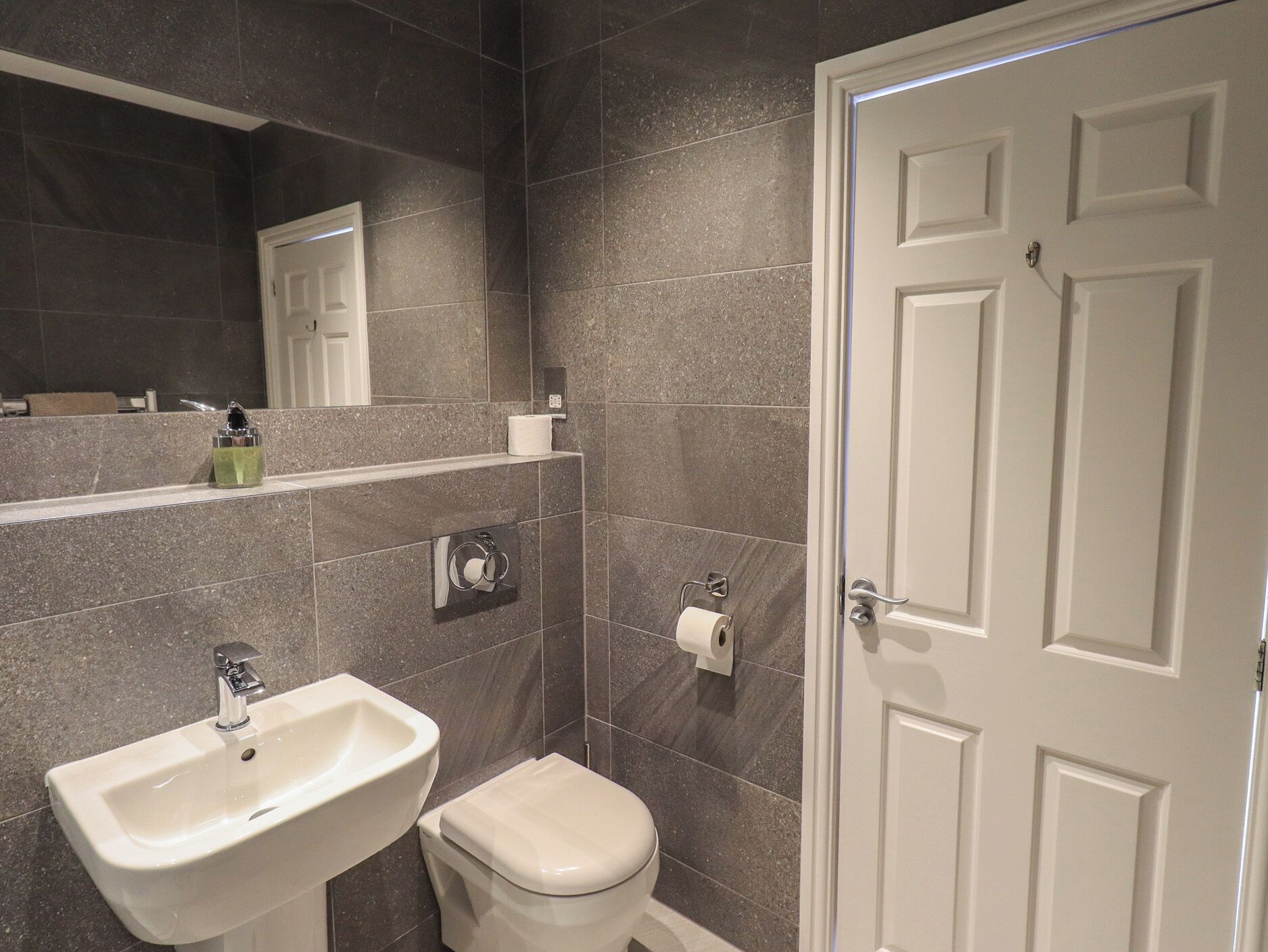A bathroom with a white sink, toilet, and a door with a mirror above the sink.