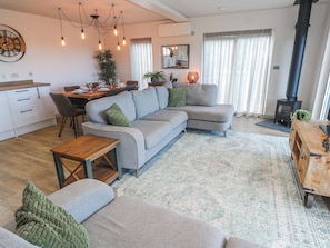 Ein modernes Wohnzimmer mit grauem Sofa, Couchtisch aus Holz und einem Essbereich mit Holztisch und Stühlen.