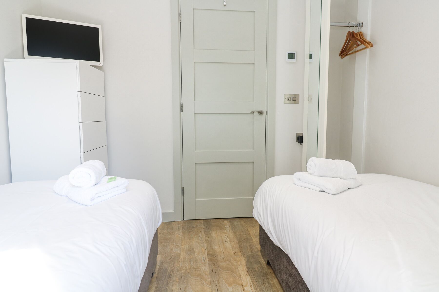 A hotel room with two beds, a wardrobe, a television, and a door.