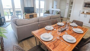 A modern living room with a sofa, a dining table set for four, and a kitchen area. - Bay View (Redruth)