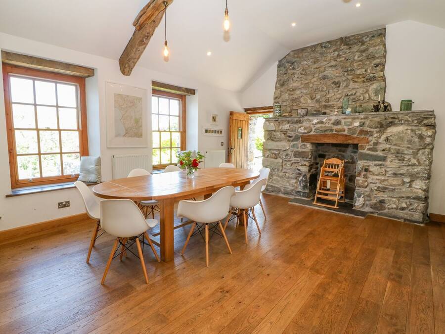 A dining area with a wooden table and chairs, a stone fireplace, and large windows.