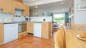 A modern kitchen with wooden cabinets, a microwave, a bread box, and a dishwasher. - Bryher (Wadebridge)