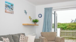 A living room with a grey sofa, a beige armchair, a wooden coffee table, and a window with a view of greenery outside. - Bryher (Wadebridge)