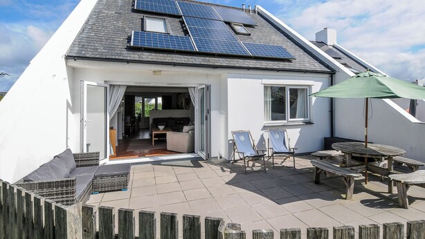 A house with solar panels on the roof, a patio with outdoor furniture, and a wooden fence. - Bryher (Wadebridge)