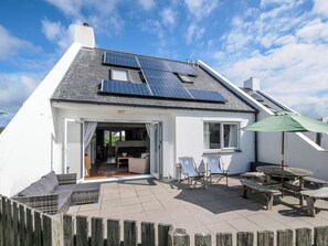 Una casa con paneles solares en el techo, un patio con mobiliario exterior y una valla de madera.