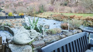 Una panchina in pietra con vista su un giardino con un ruscello, circondata da rocce e vegetazione.