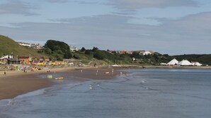 A beach with a sandy shore, a few people, and buildings in the background. - The Corner House (Scarborough)