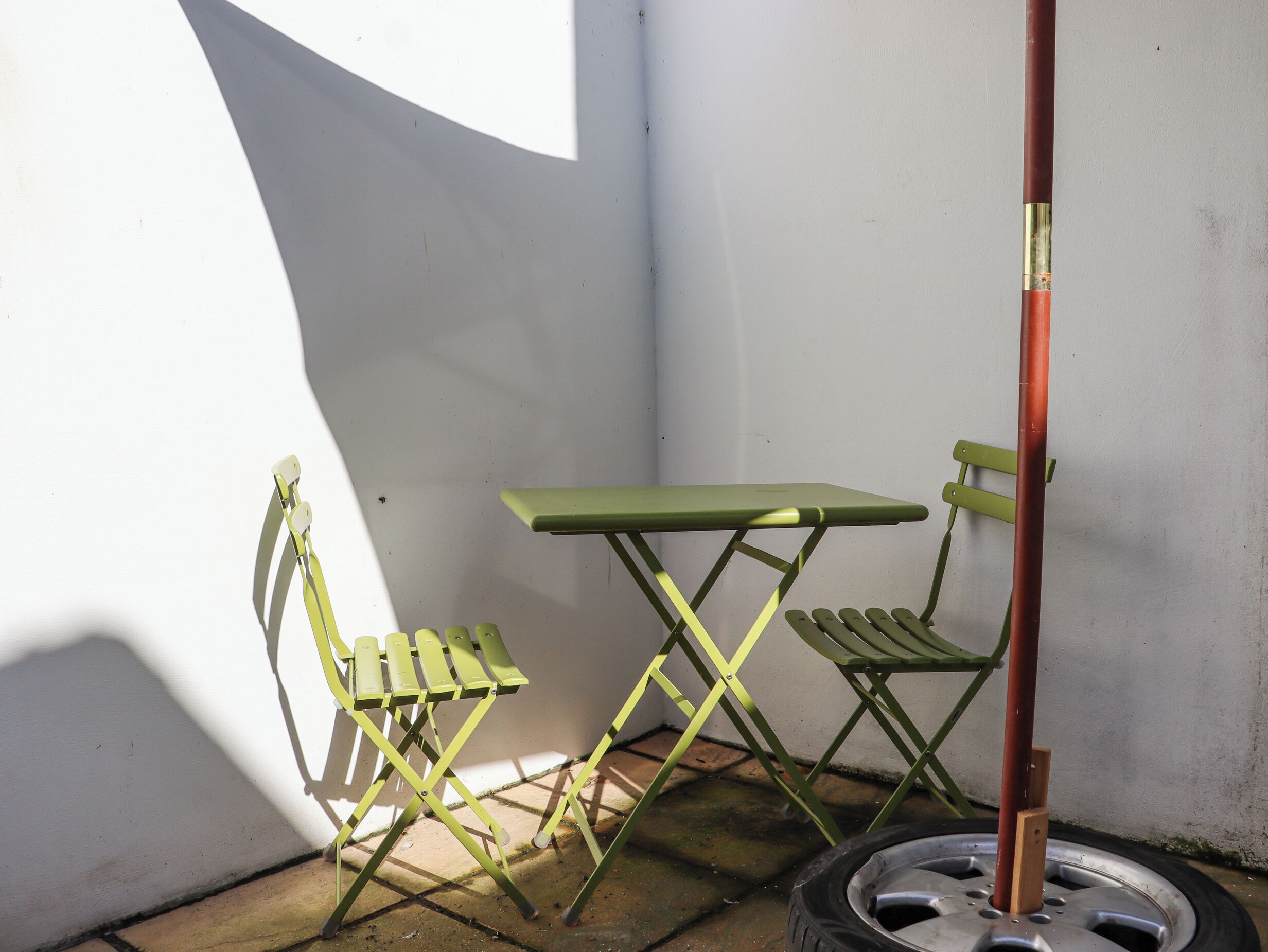 A small outdoor area with a green metal table and chair, a metal pole, and a car tire.