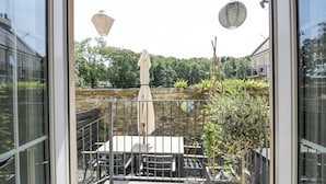 Une terrasse avec une table et des chaises, une lanterne suspendue, et une vue sur un mur de pierre et de la verdure.