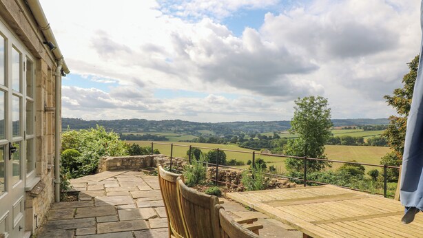A stone pathway leading to a wooden bench and table, overlooking a rural landscape with fields and hills. - Ivy Cottage (Chippenham)
