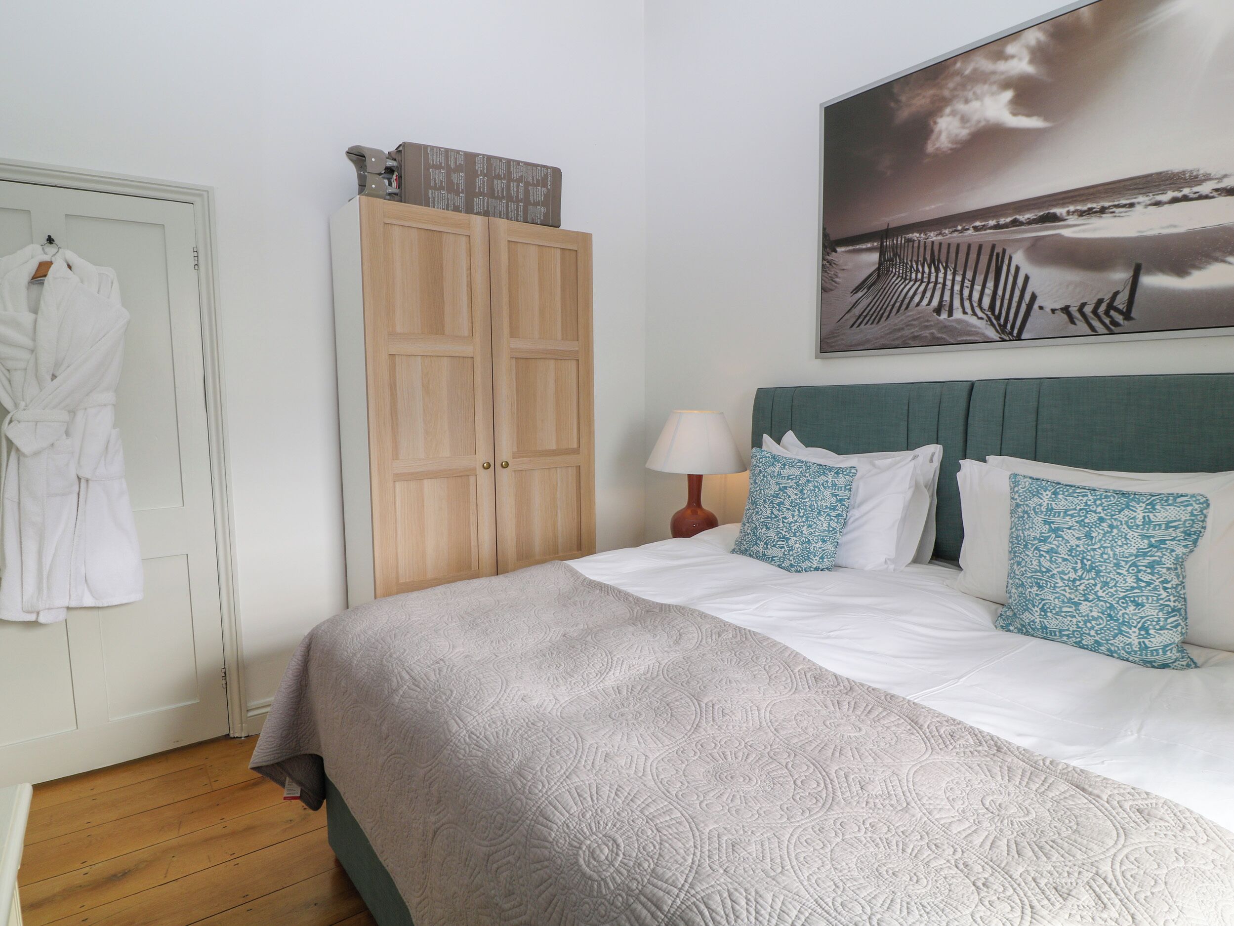 A bedroom with a bed, a wardrobe, a painting, and a robe hanging on the door.