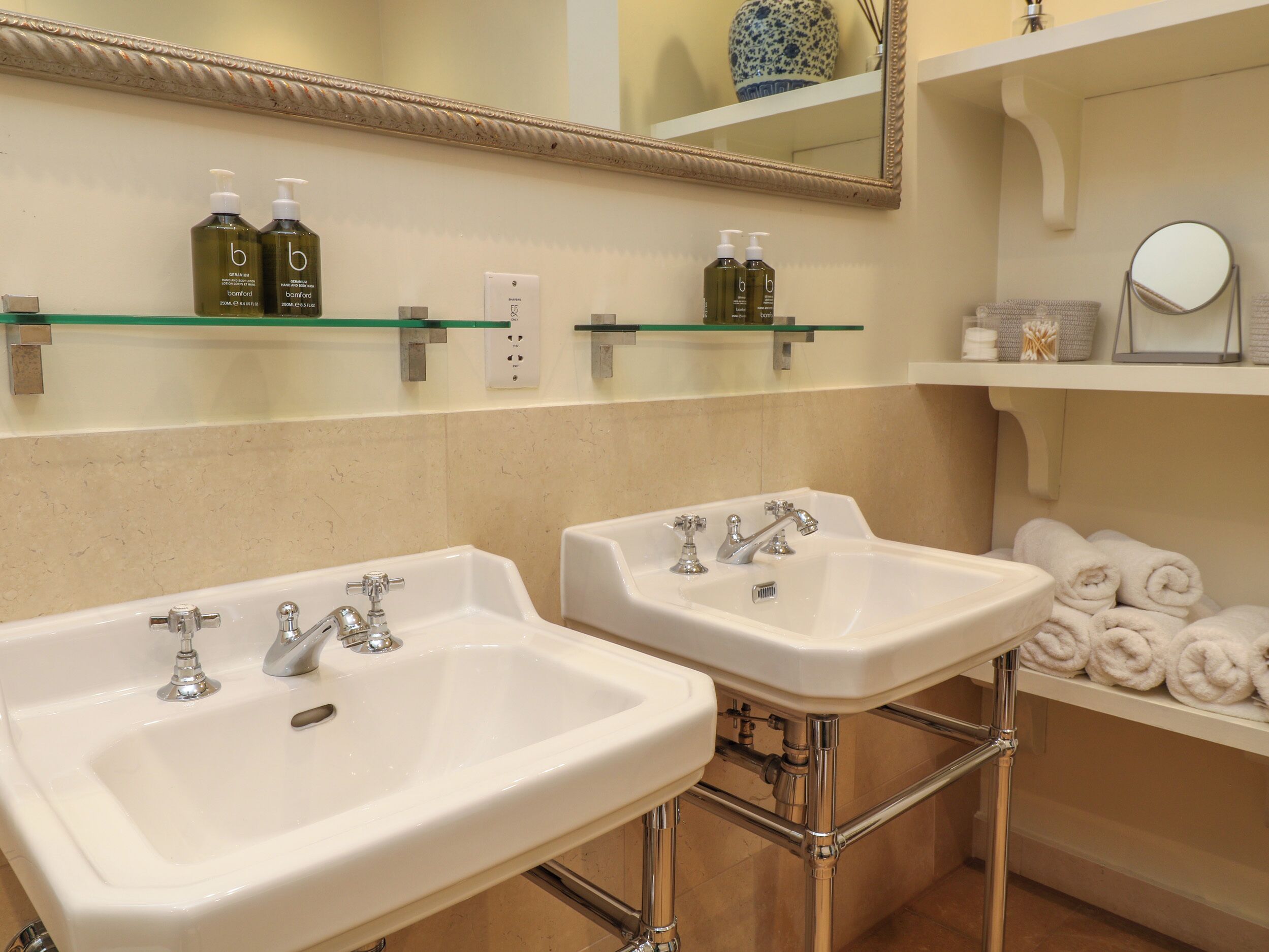A bathroom with two sinks, a mirror, and shelves with toiletries.