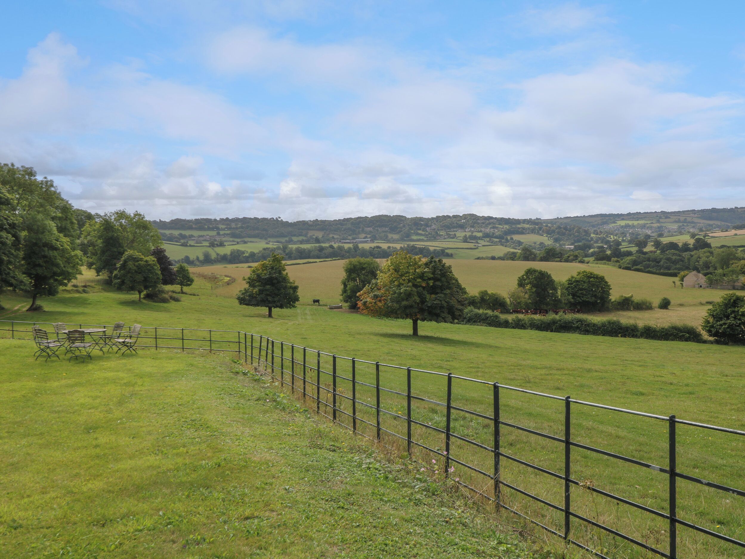 A rural landscape with a fenced area, trees, and rolling hills in the background.