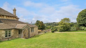 A stone building with a sloped roof and a chimney, surrounded by a grassy field and trees. - Ivy Cottage (Chippenham)