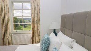A bedroom with a bed, a window with curtains, a radiator, and a bedside lamp. - Ivy Cottage (Chippenham)