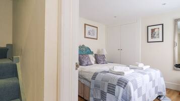 Een slaapkamer met een bed, nachtkastje, dressoir en een deur naar een trap.