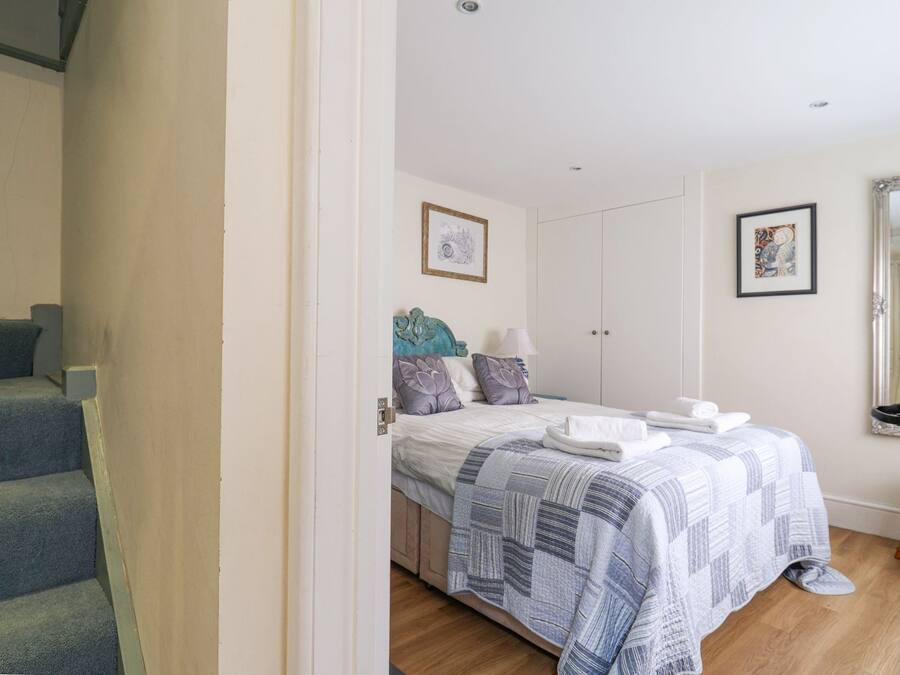 Een slaapkamer met een bed, nachtkastje, dressoir en een deur naar een trap.