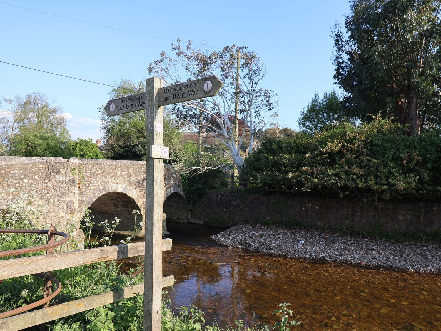 Un segnale di legno con frecce direzionali, un ponte in pietra e un corso d'acqua limpido.