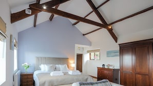 A bedroom with a large bed, a smaller bed, a sofa, wooden beams on the ceiling, a dresser, and a window with a view.