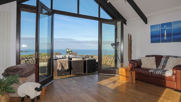 A spacious living room with a large glass door leading to a balcony with a view of the sea.