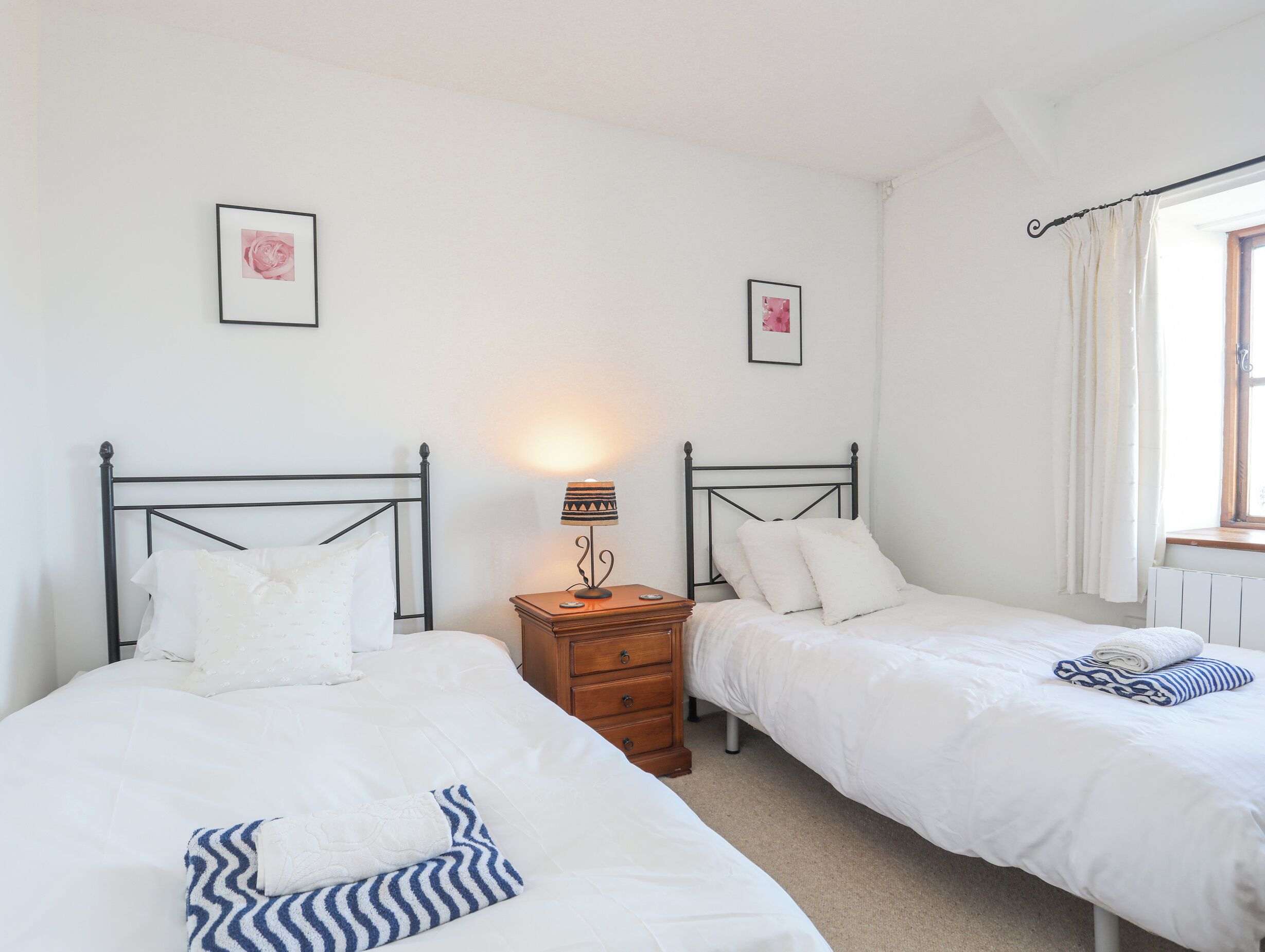 Une chambre avec deux lits simples, une table de chevet avec une lampe et une fenêtre avec des rideaux.