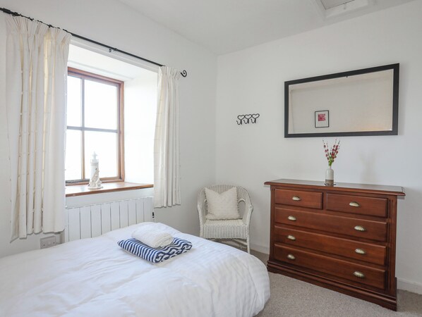 Une chambre à coucher comprenant un lit, une commode, une chaise, une fenêtre avec des rideaux et un cadre photo fixé au mur.