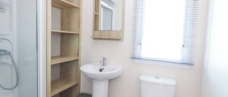 A bathroom with a glass shower enclosure, a white sink, a toilet, and a window with blinds.