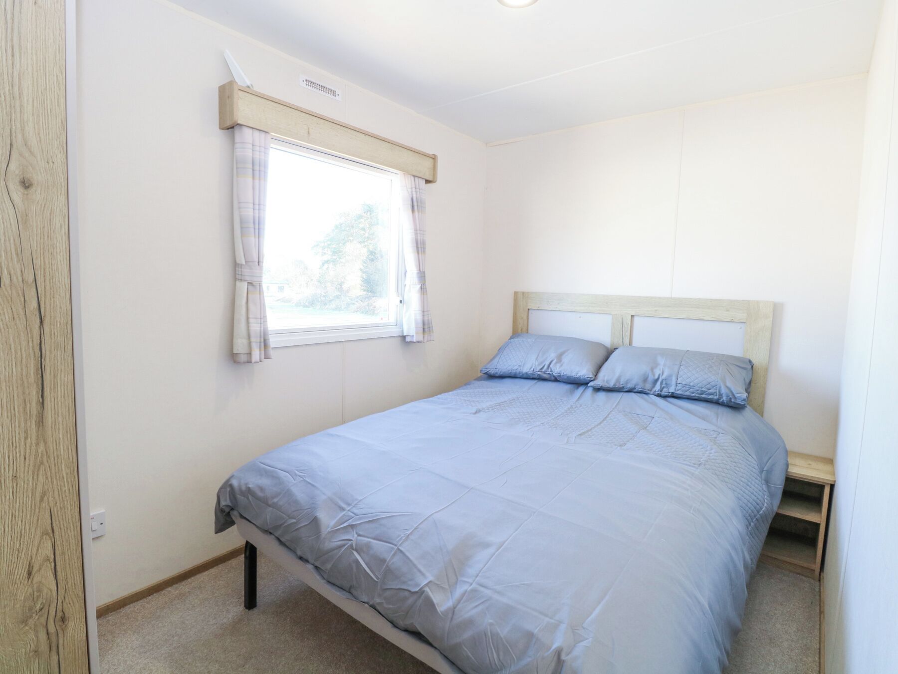 A bedroom with a single bed, a window with curtains, and a wooden headboard.