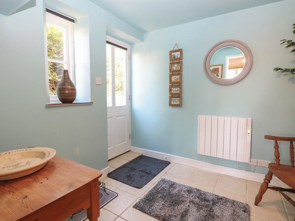 Une pièce avec une table en bois, un vase, une porte, un miroir, un radiateur et un tapis.