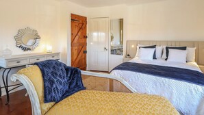 A bedroom with two beds, a dresser, a mirror, and a door. - Cobble Cottage (Fakenham)