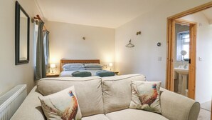 A bedroom with a bed, a wooden door, a bathroom with a sink, and a living area with a sofa and cushions. - B&B 3 (Saffron Walden)