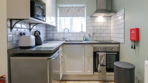 A compact kitchen with white cabinets, a microwave, a toaster, a sink, and a stove. - B&B 3 (Saffron Walden)