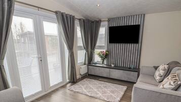 Una sala de estar moderna con un sofá gris, un televisor de pantalla plana montado en la pared y un ventanal con persianas.