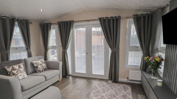 A modern living room with a grey sofa, a patterned rug, and grey curtains. - 24 Sherwood (Carnforth)