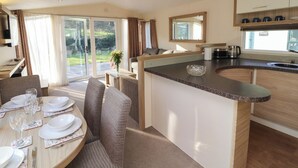 A modern kitchen with a central island, dining area with a table set for four, and a sliding glass door leading to a garden.