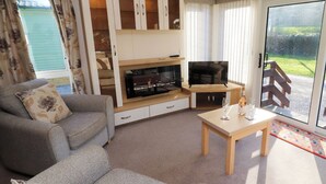Ein Wohnzimmer mit einer Couch, einem Fernseher und einem Tisch mit Gläsern und einer Flasche.
