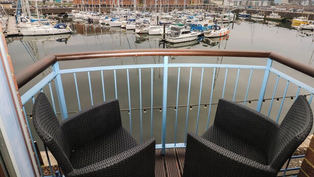 Un balcón con sillas de mimbre con vista a una marina con varios barcos.