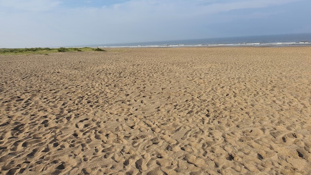 Uma extensa praia de areia com pegadas que se estendem em direção ao oceano.