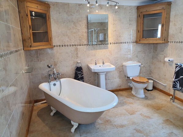 A bathroom with a freestanding bathtub, a sink, a toilet, and wooden cabinets. - The Beaches, 23 Trusthorpe Road (Mablethorpe)