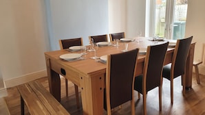Uma sala de jantar com uma mesa de madeira posta para seis pessoas, rodeada por cadeiras e um banco no final.
