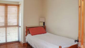 A small, single-bed room with wooden flooring, a wooden headboard, and a red pillow.