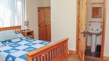 A bedroom with a wooden bed, a nightstand with a lamp, a wardrobe, and a bathroom with a sink and mirror.