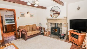 A cozy living room with a fireplace, a sofa, a television, and a wooden table with a notebook. - Brook Cottage (High Peak)