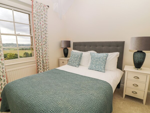 Een slaapkamer met een bed, twee nachtkastjes, een raam met gordijnen en uitzicht op het platteland.