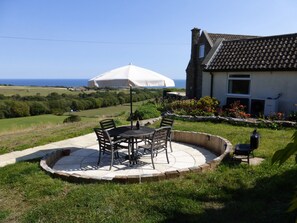 Um pátio com mesa e cadeiras, um guarda-sol branco e vista para o mar.