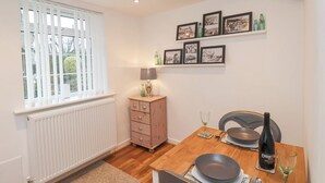 A dining area with a wooden table set for two, a radiator, a small cabinet, and framed pictures on the wall. - Meadow Cottage (Scarborough)