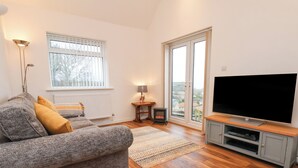 A living room with a grey sofa, a flat-screen TV, a wooden floor, a radiator, and a window with blinds. - Meadow Cottage (Scarborough)