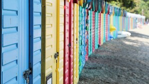 Una fila di armadietti colorati, probabilmente per spiaggia o piscina, con sabbia sotto e alberi sullo sfondo.